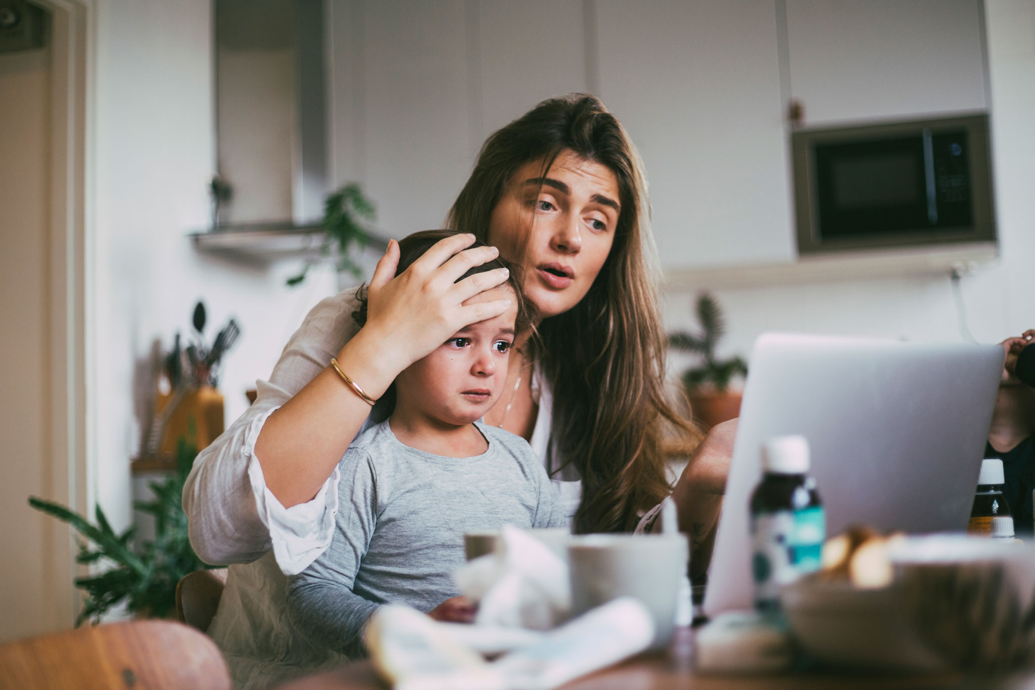 Attentive mother holding her sick child while on a telehealth call while at home.