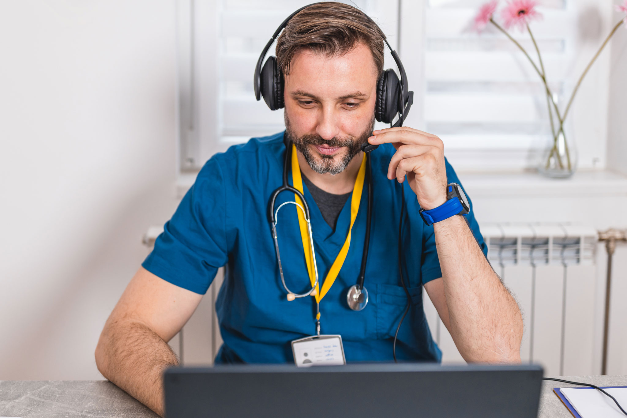 From his office, a male nurse conducts a telehealth session using his laptop and headphones, demonstrating the effectiveness of remote patient care