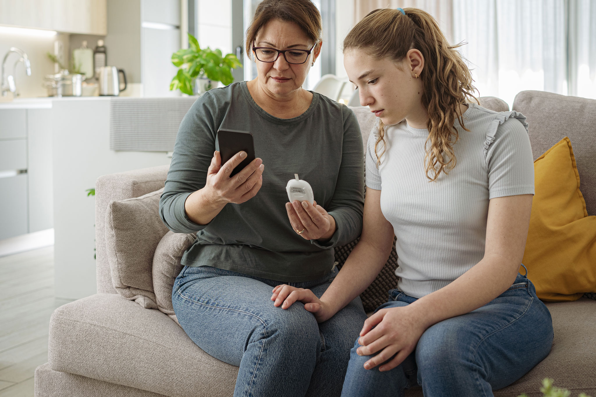 Mother and teenager daughter using phone and glocometer to check blood sugar level of the girl. High resolution 42Mp indoors digital capture taken with SONY A7rII and Zeiss Batis 40mm F2.0 CF lens